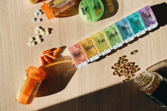 Pastilier săptămânal deschis lângă un pahar cu apă pe masă